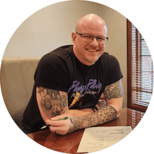 Tattooed man smiling while seated at a table, headshot
