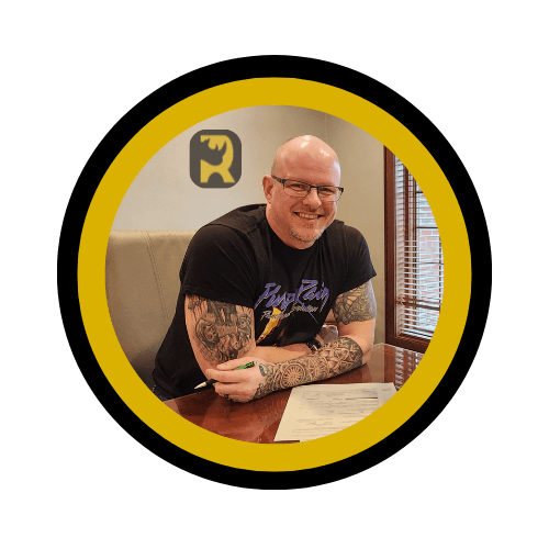 Circular badge photo of tattooed man smiling at a table, with rhino icon